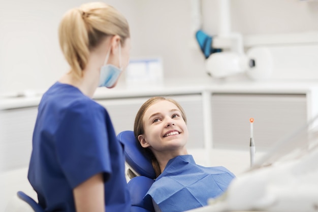 concept de personnes, de médecine, de stomatologie et de soins de santé - femme dentiste heureuse avec une patiente parlant au bureau de la clinique dentaire