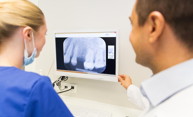concept de personnes, de médecine, de stomatologie et de soins de santé - gros plan sur un dentiste et un assistant regardant des rayons X sur l'écran du moniteur à la clinique dentaire