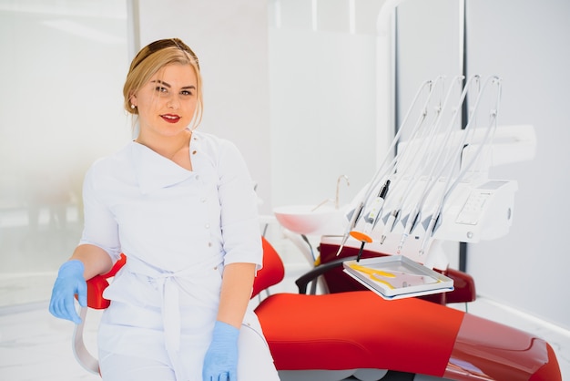 Concept de personnes, médecine, stomatologie et soins de santé - heureuse jeune femme dentiste avec des outils sur fond de cabinet médical