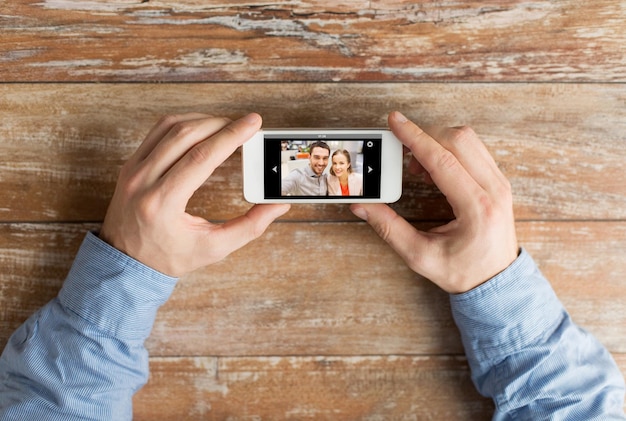 concept de personnes, de mémoire, de relations et de technologie - gros plan de mains masculines tenant un smartphone avec photo d'un couple heureux à l'écran à table