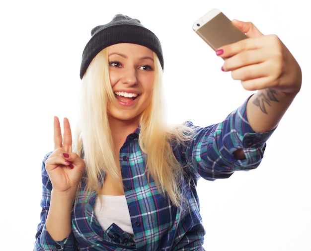 Concept de personnes, de mode de vie et de technologie : jolie adolescente portant un chapeau, prenant des selfies avec son téléphone intelligent - isolé sur blanc