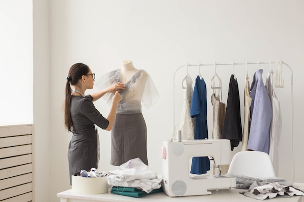 Concept de personnes et de mode - Vue arrière du propriétaire du magasin de mode vêtu d'une tenue élégante mesurant des matériaux sur un mannequin au bureau.
