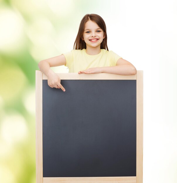 concept de personnes, de publicité et d'éducation - petite fille heureuse pointant le doigt vers le tableau noir