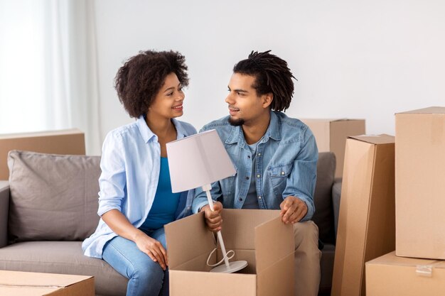 concept de personnes, de réparation et d'immobilier - couple souriant avec des boîtes en carton et une lampe entrant ou sortant de la maison