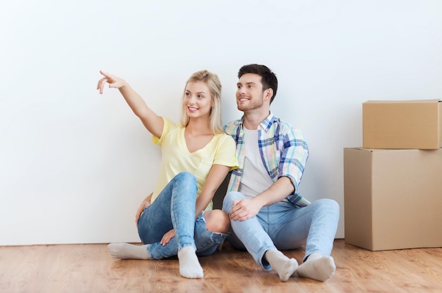 concept de personnes, de réparation et d'immobilier - couple souriant avec des boîtes déménageant dans une nouvelle maison et rêvant