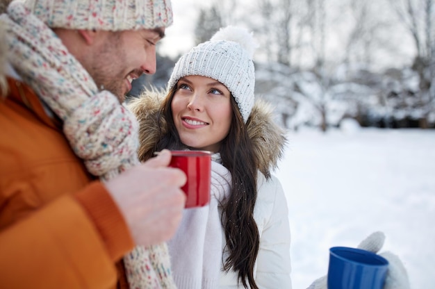Concept de personnes, de saison, d'amour, de boissons et de loisirs - couple heureux tenant des tasses de thé chaud sur le paysage d'hiver