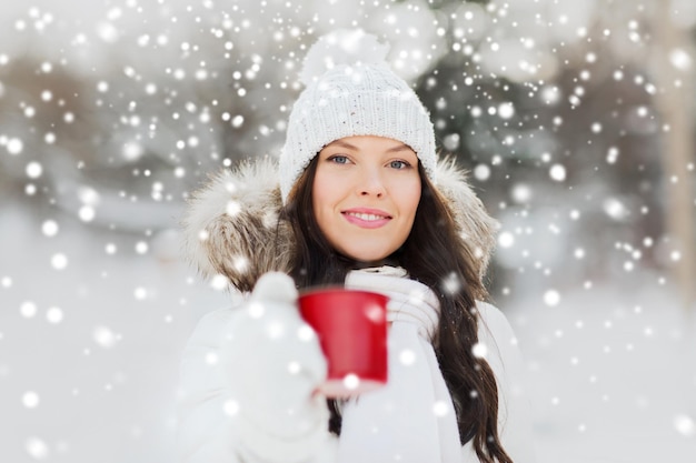 concept de personnes, de saison, de boissons et de loisirs - jeune femme heureuse avec une tasse de thé à l'extérieur en hiver