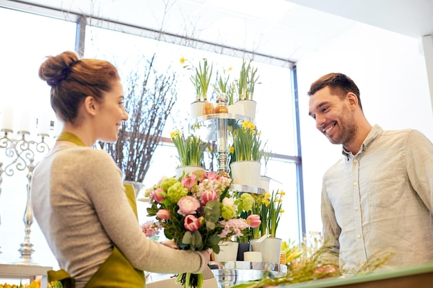 concept de personnes, de shopping, de vente, de fleuristerie et de consommation - femme fleuriste souriante heureuse faisant un bouquet pour et homme ou client au fleuriste