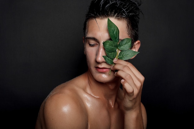 Concept de personnes, de soins de la peau et de beauté - Jeune homme mouillé aux cheveux noirs sur fond noir. Portrait masculin avec poitrine rasée. Soins de la peau des hommes. Homme beau musclé déchiré sur fond noir