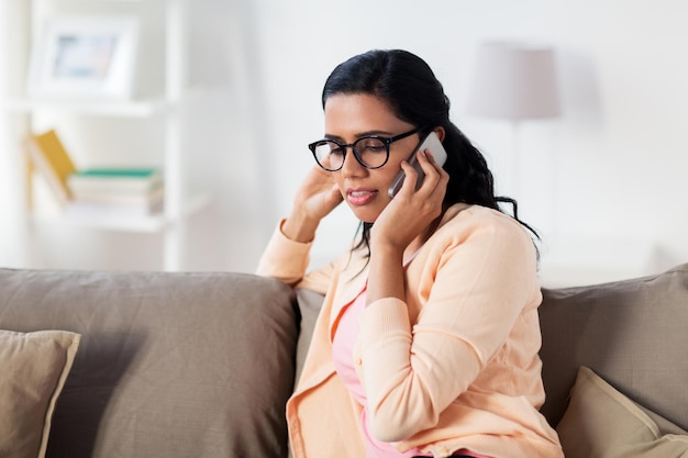 concept de personnes, de technologie, de communication et de loisirs - heureuse jeune femme indienne dans des lunettes appelant sur un smartphone à la maison