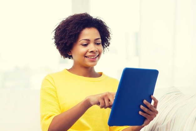 concept de personnes, de technologie et de loisirs - heureuse jeune femme afro-américaine assise sur un canapé avec un ordinateur tablette pc à la maison