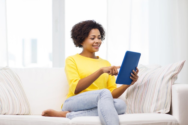 concept de personnes, de technologie et de loisirs - heureuse jeune femme afro-américaine assise sur un canapé avec un ordinateur tablette pc à la maison