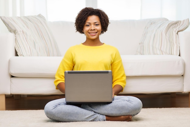 concept de personnes, de technologie et de loisirs - heureuse jeune femme afro-américaine assise sur le sol avec un ordinateur portable à la maison