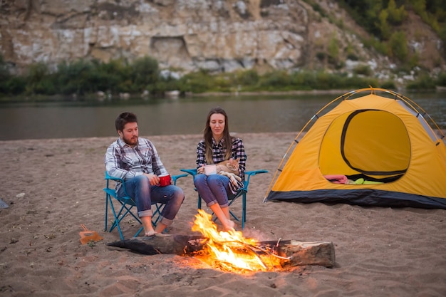 Concept de personnes, de tourisme et de nature - L'homme et la femme avec leur chat sont assis près d'un feu.