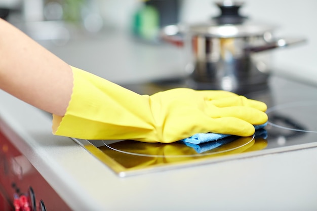 concept de personnes, de travaux ménagers et d'entretien ménager - gros plan sur une main de femme dans un gant de protection avec une cuisinière de nettoyage de chiffon à la cuisine à domicile