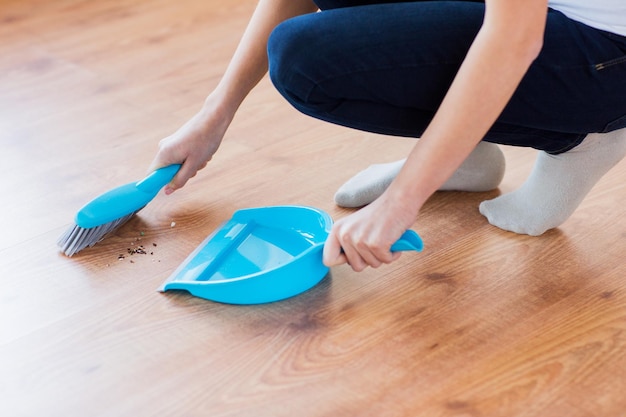 concept de personnes, de travaux ménagers, de nettoyage et d'entretien ménager - gros plan d'une femme avec une brosse et une pelle à poussière balayant le sol à la maison