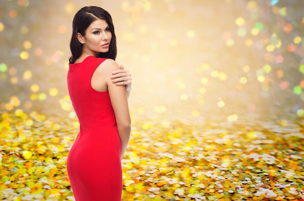 concept de personnes, vacances, noël et glamour - belle femme sexy en robe rouge sur fond de paillettes dorées ou de lumières jaunes