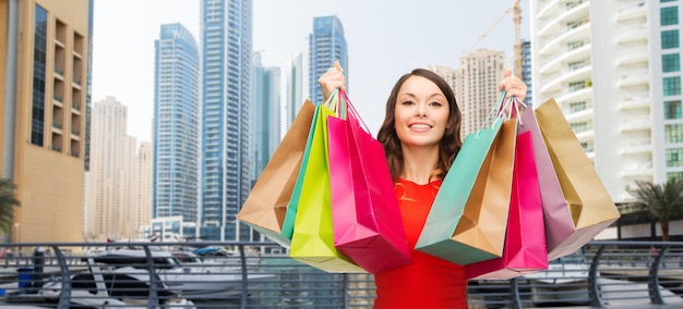 concept de personnes, vacances, tourisme, voyage et vente - jeune femme heureuse avec des sacs à provisions sur fond de gratte-ciel de la ville de dubaï