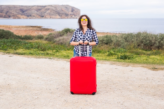 Concept de personnes, de vacances et de voyage - belle jeune femme debout avec une valise sur le mur de la mer.