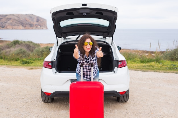 Concept de personnes, de vacances et de voyage - jeune femme avec valise montrant les pouces vers le haut à l'extérieur.