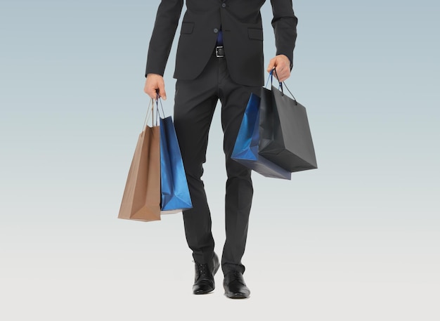 concept de personnes, de vente, de mode et de consommation - gros plan d'un homme en costume avec des sacs à provisions sur fond bleu