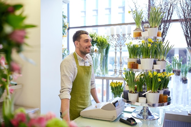 concept de personnes, de vente, de vente au détail, d'entreprise et de fleuristerie - homme fleuriste souriant heureux avec une caisse debout au comptoir du magasin de fleurs