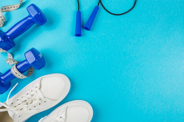 Le concept de perte de poids dans les sports de remise en forme Vue de dessus photo de chaussures de sport blanches ruban à mesurer et haltères bleus sur fond bleu pastel isolé avec espace videMode de vie sain