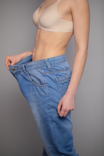 Concept de perte de poids. Jeune femme montre sa perte de poids et porte ses vieux jeans. Slim femme en Big Jeans montrant comment elle perdait du poids