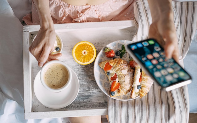 Concept petit-déjeuner au lit croissant aux fraises et à la crème sur un plateau en bois clair avec une tasse de café