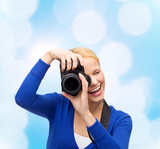 concept de photographie, de technologie et de personnes - jeune femme souriante prenant une photo avec un appareil photo numérique sur fond de lumières bleues