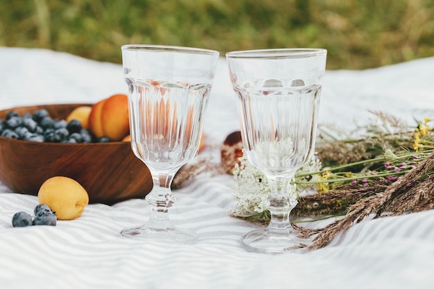 Concept de pique-nique et de vacances d'été Délicieux fruits et baies verres à vin et bouquet de fleurs sauvages sur couverture bleuets pêches et abricots