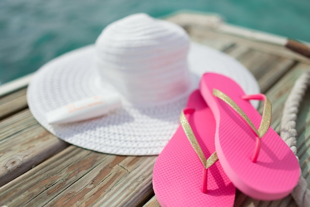 concept de plage, d'été, de vacances et d'accessoires - gros plan sur un chapeau, un écran solaire et des chaussons au bord de la mer