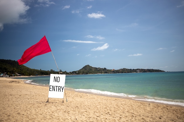 concept plage fermée, plage privée, ne fonctionne pas. il y a un drapeau rouge et un panneau disant pas d'entrée sur une plage tropicale vide un beau jour