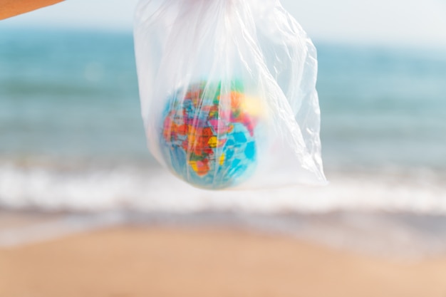 Concept de pollution de l'environnement. Femme tenant dans ses mains un sac en plastique et la planète Terre sur fond de mer.