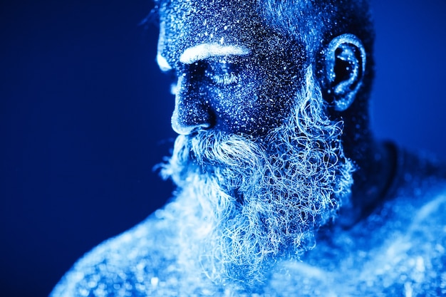Concept. Portrait d'un homme barbu. L'homme est peint en poudre ultraviolette.