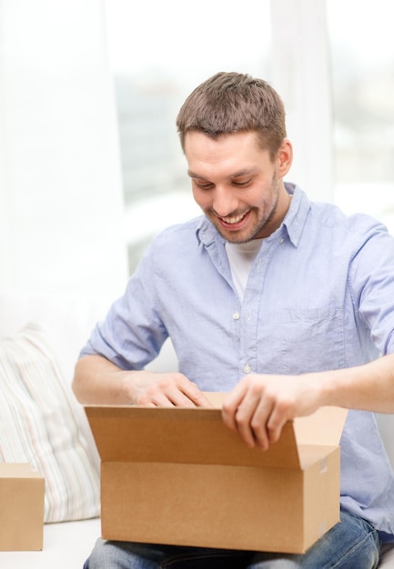 concept de poste, de maison et de style de vie - homme souriant avec des boîtes en carton à la maison