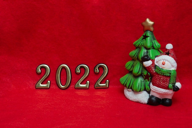 Concept pour la carte du Nouvel An, l'invitation et l'emballage sur un fond rouge en tissu un bonhomme de neige avec un arbre de Noël et des nombres d'or 2022.Bannière.