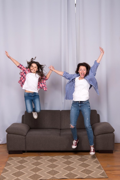 Concept de pouvoir des filles Célébrer la journée de la femme Filles seulement Amis de maman et fille Mère fille joyeuse sautant canapé Enfance heureuse Filles s'amusant Enfant et maman jouent ensemble Bonheur amusant