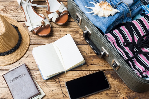 Concept de préparatifs de voyage avec valise, vêtements et accessoires sur une vieille table en bois. Vue de dessus Espace de copie