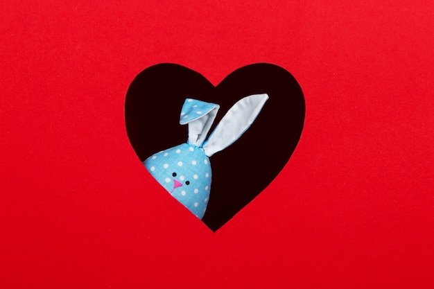Le concept de printemps, joyeuses Pâques, lapin bleu à l'oreille à la main, sortir d'un trou en forme de coeur sur fond rouge. Copiez l'espace.