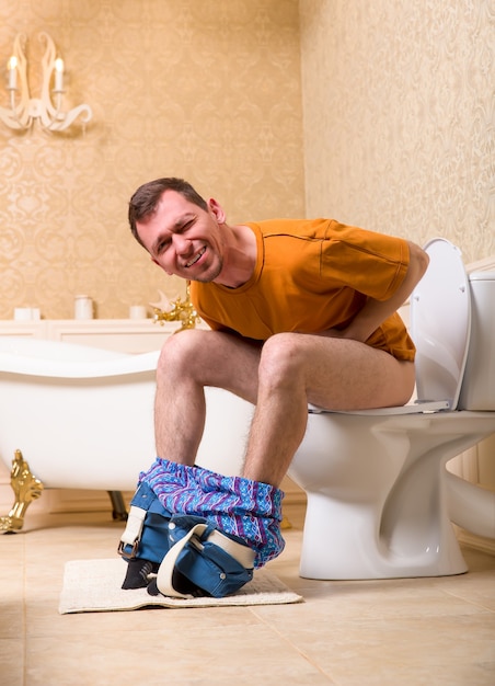 Concept de problème de diarrhée. Homme avec un pantalon assis sur la cuvette des toilettes