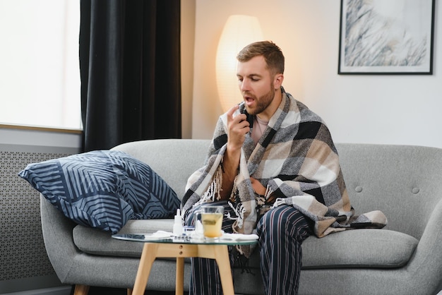 Concept de problème de personnes et de santé malheureux homme malade pulvérisant sa gorge avec un spray oral au lit à la maison