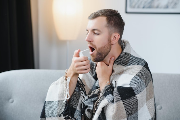 Concept de problème de personnes et de santé malheureux homme malade pulvérisant sa gorge avec un spray oral au lit à la maison