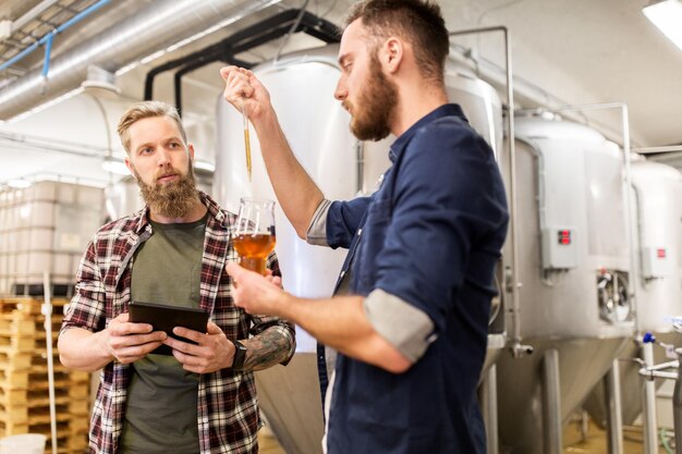 concept de production, de fabrication, d'affaires et de personnes d'alcool - hommes avec pipette et tablette PC testant de la bière artisanale à la brasserie