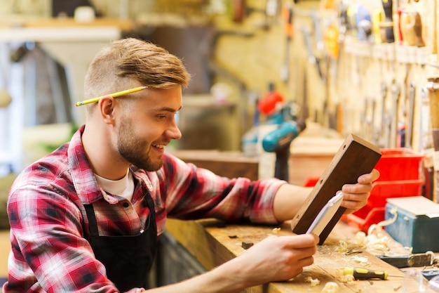 concept de profession, de menuiserie, de menuiserie et de personnes - charpentier avec planche de bois et cahier vérifiant ses notes à l'atelier