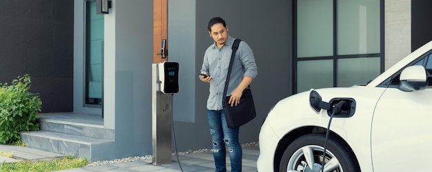 Concept progressif d'homme asiatique et de voiture électrique avec borne de recharge à domicile