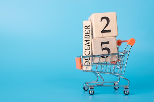 Concept de promotion d'offre de réduction de Noël. Profil latéral photo en gros du panier transportant des cubes avec la date du 25 décembre isolée sur fond bleu