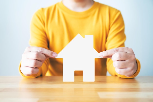 Concept de protection de la maison d'assurance Les mains de l'homme protègent l'icône de la maison sur la table en bois