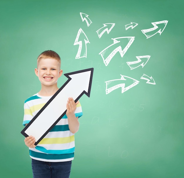 Photo concept de publicité, de direction, d'éducation et d'enfance - petit garçon souriant avec une flèche blanche pointant vers le haut sur un tableau vert avec fond de griffonnages