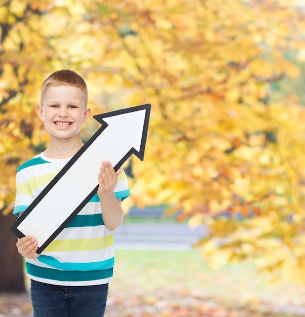 Photo concept de publicité, de direction et d'enfance - petit garçon souriant avec une flèche blanche pointant vers le haut sur fond de parc d'automne